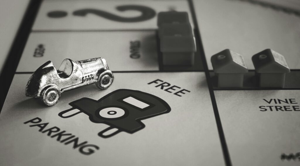 Stylized black and white close-up of Monopoly game pieces on the Free Parking space.